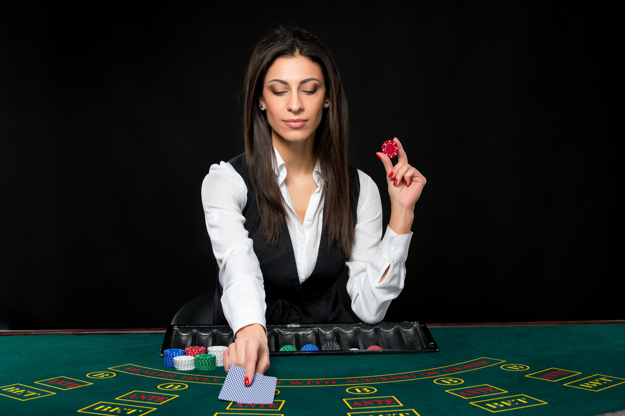 A female croupier is seen at a casino table dealing cards and holding chips. Live Dealer is Over 50% of Online Table Game Revenue in PA
