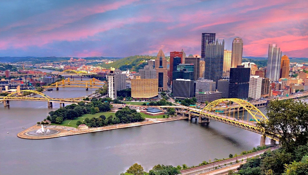 Pittsburgh skyline is seen at sunset. Land with buildings and skyscrapers juts out with water and bridges on either side. The sky is a pretty pink and blue. With Michigan joining the interstate online poker agreement this week, eyes turn to Pennsylvania.